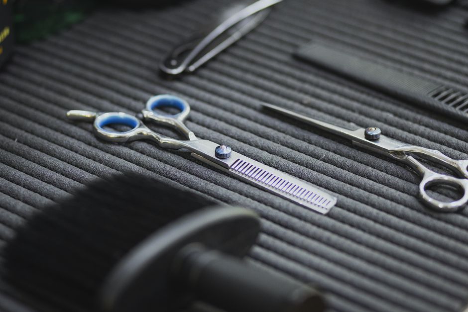 Close-up of hairdressing scissors and combs on a textured surface for salon use.