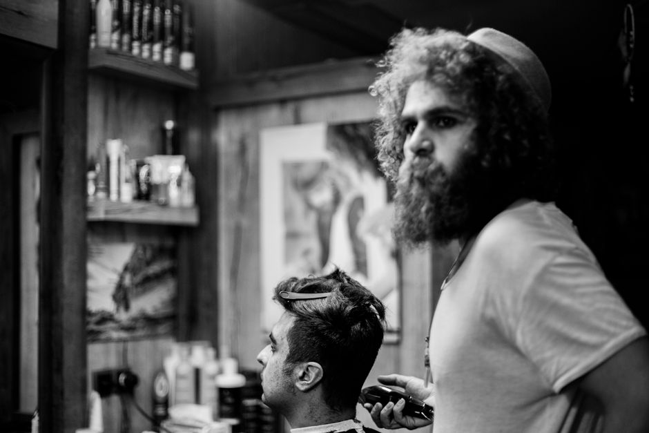 Artistic black and white photo of a barber crafting a hairstyle in a vintage barbershop setting.